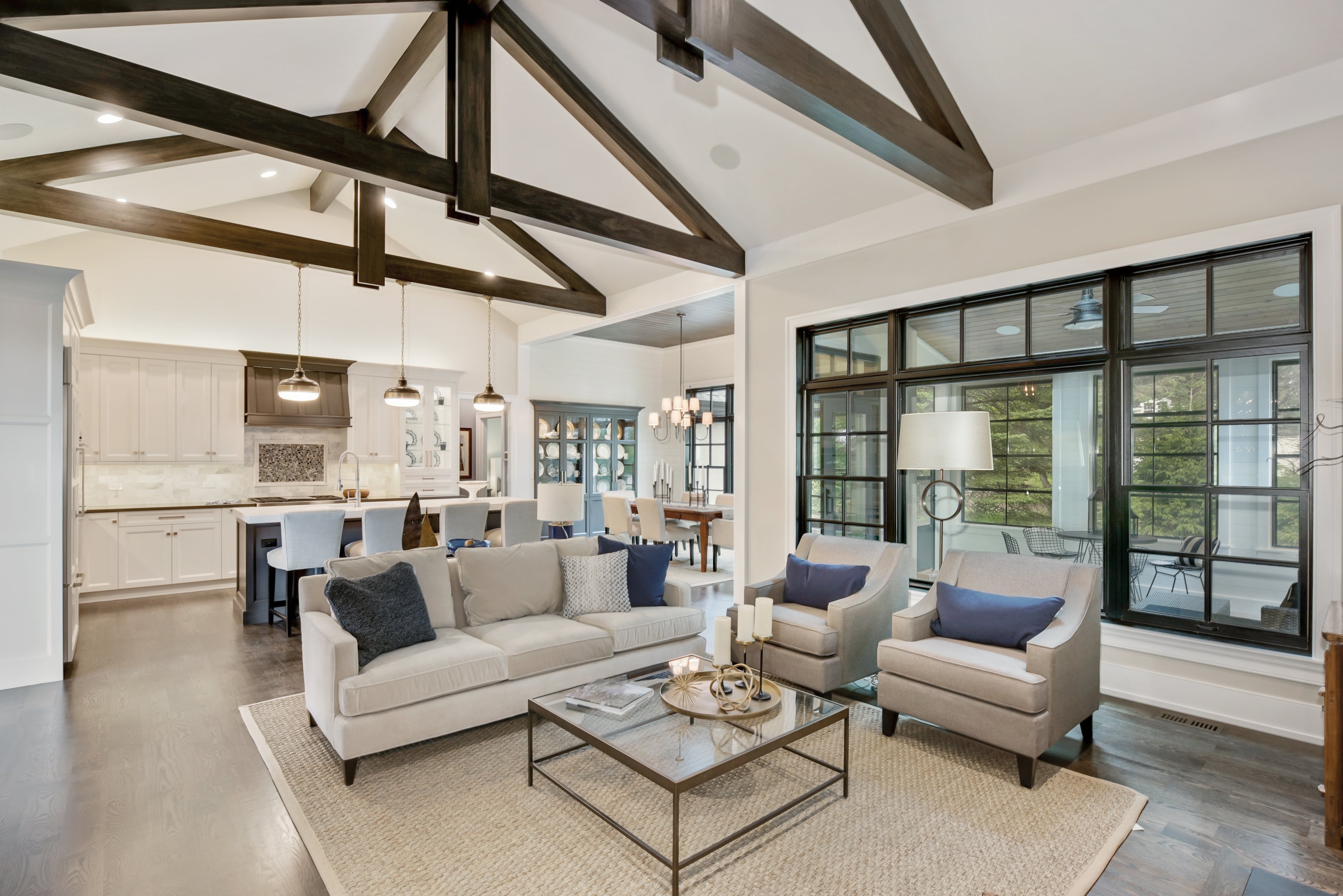 Spacious open-plan living area with a modern design, featuring a cozy seating arrangement, exposed beams, and large windows for ample natural light