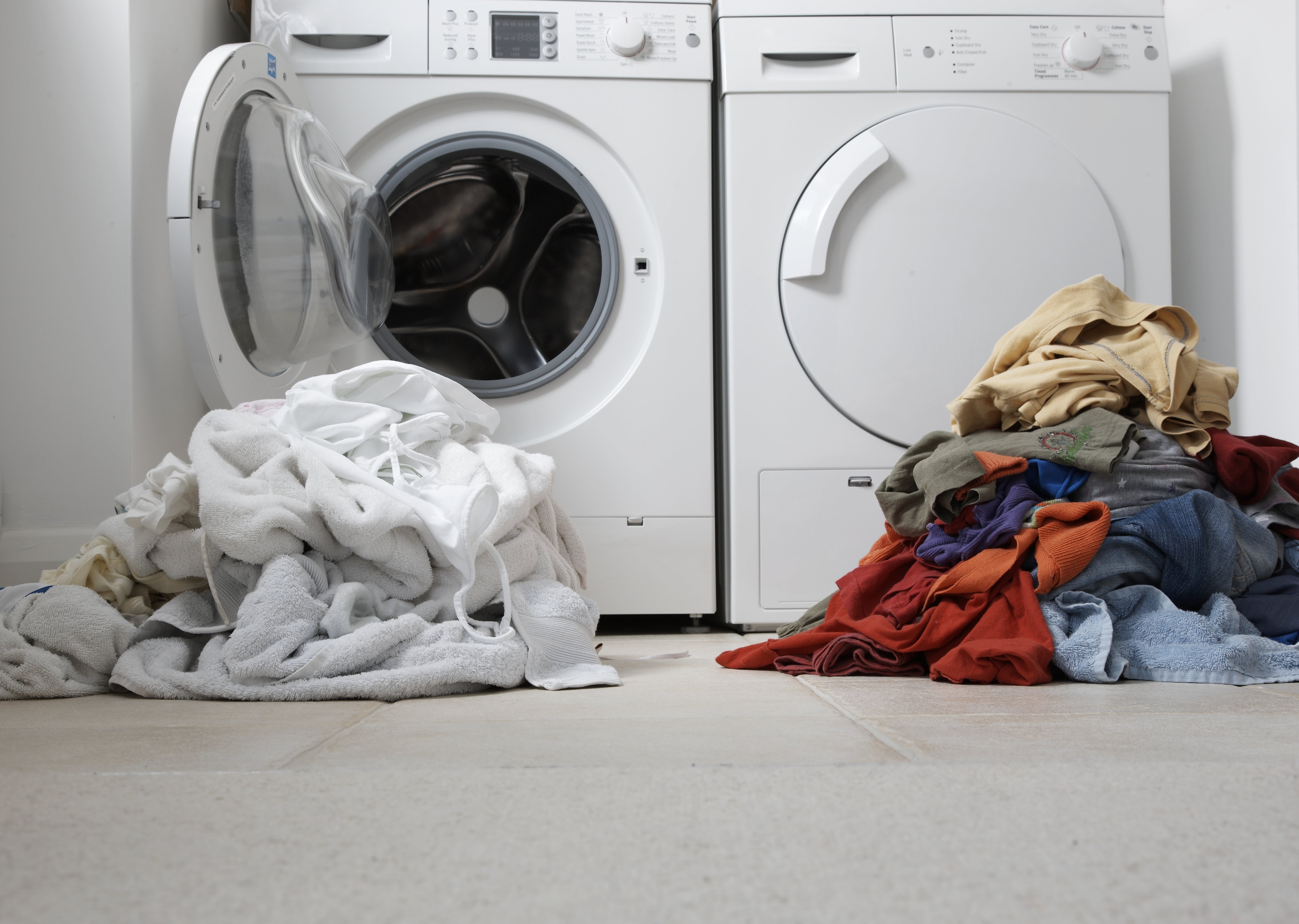 Laundry room with a washing machine, dryer, and piles of white and colored clothes on the floor