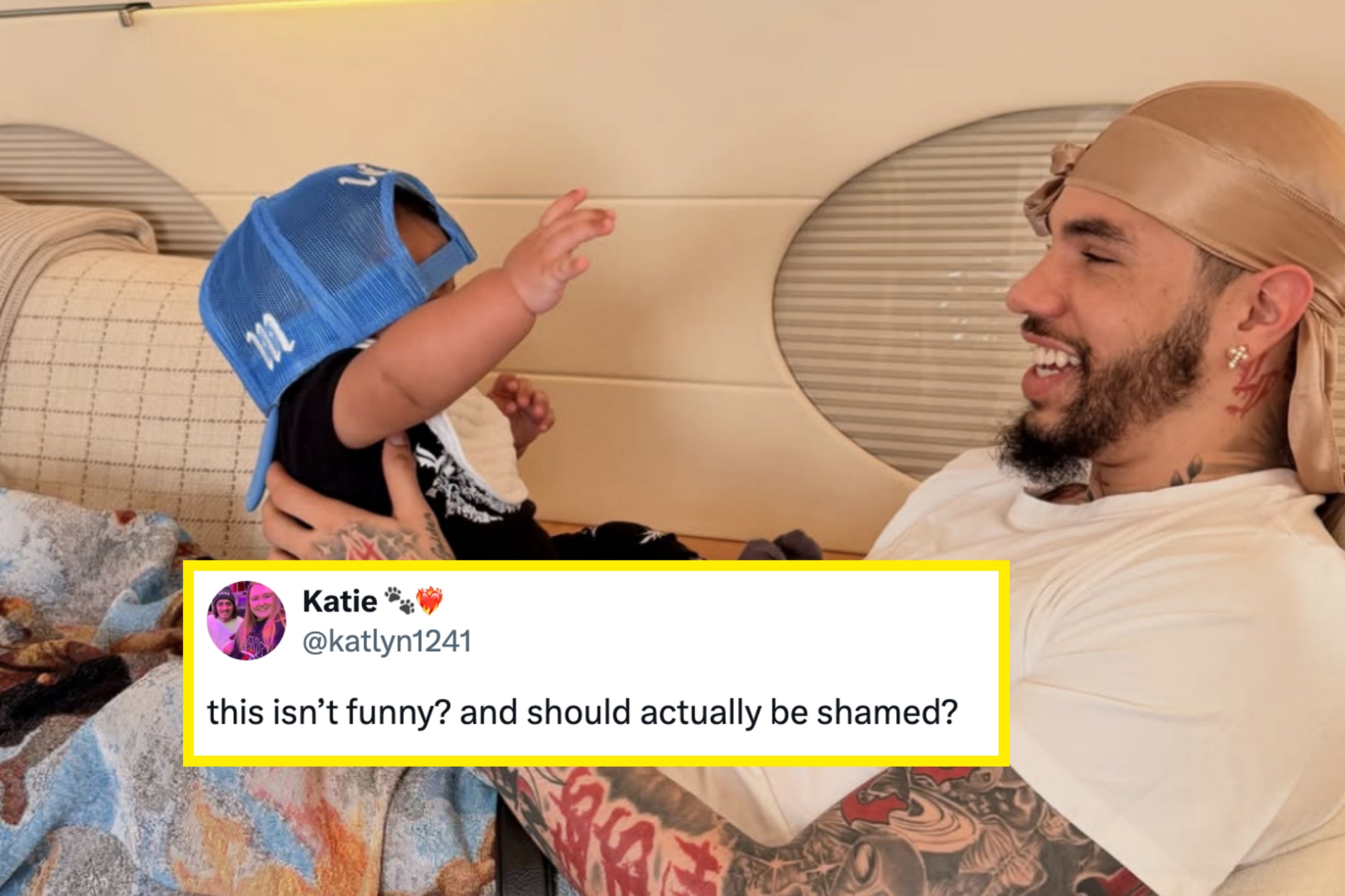 A person with tattoos and a durag smiles at a baby wearing a cap, sitting on their lap in an airplane cabin