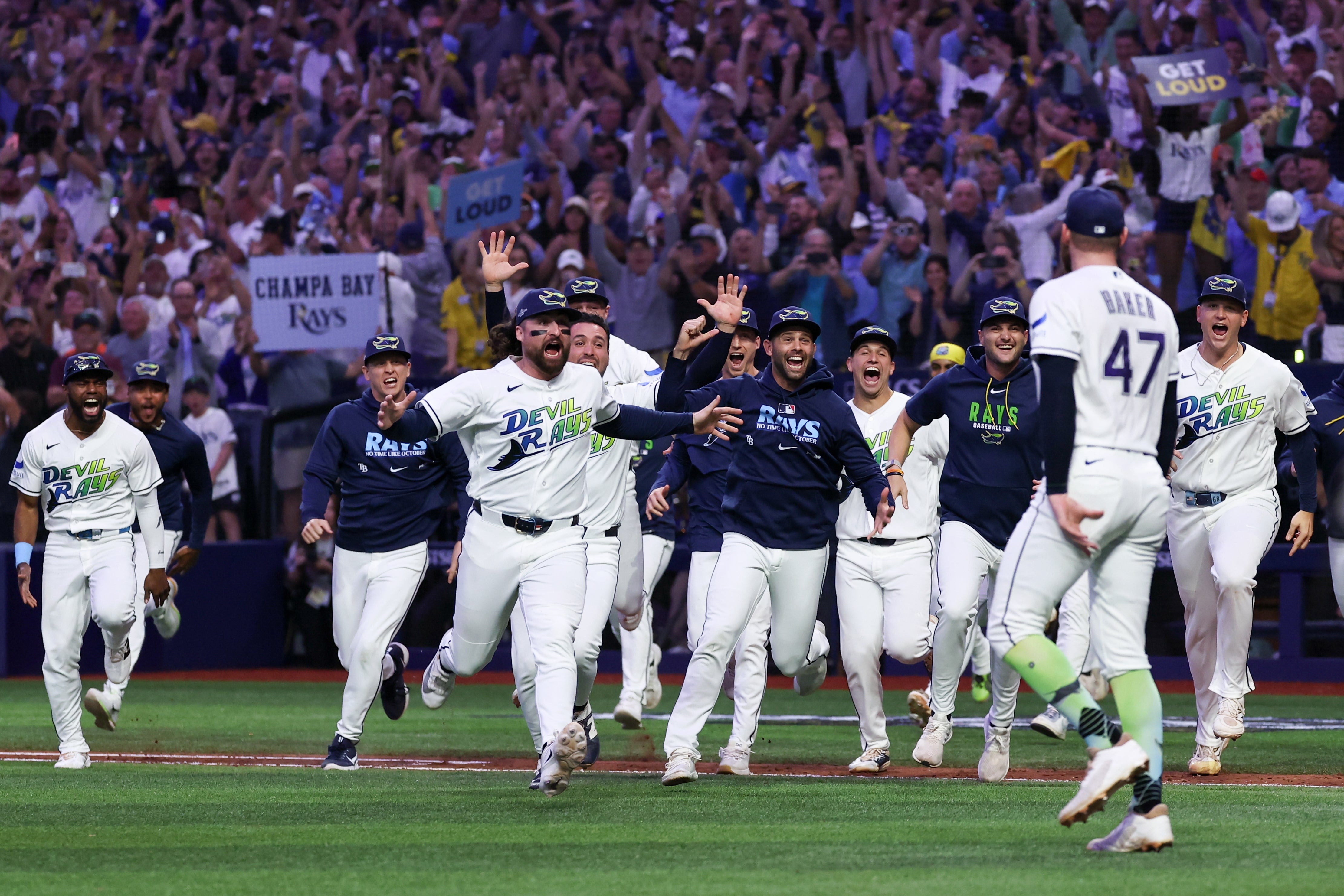 Baseball squad celebrating connected field, moving towards subordinate with fig 47. Crowd successful inheritance holds "Get Loud" and "Champa Bay Rays" signs