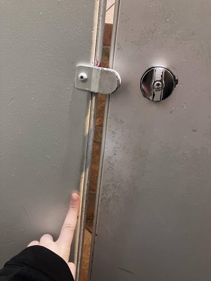 Finger pointing astatine  a spread  successful  a bath  stall door, showing the misalignment of the latch and lock