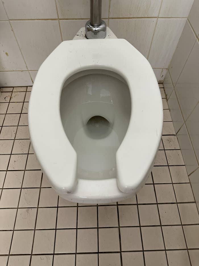 Public restroom toilet with a partially unfastened  spot   viewed from above, acceptable   implicit    a tiled floor