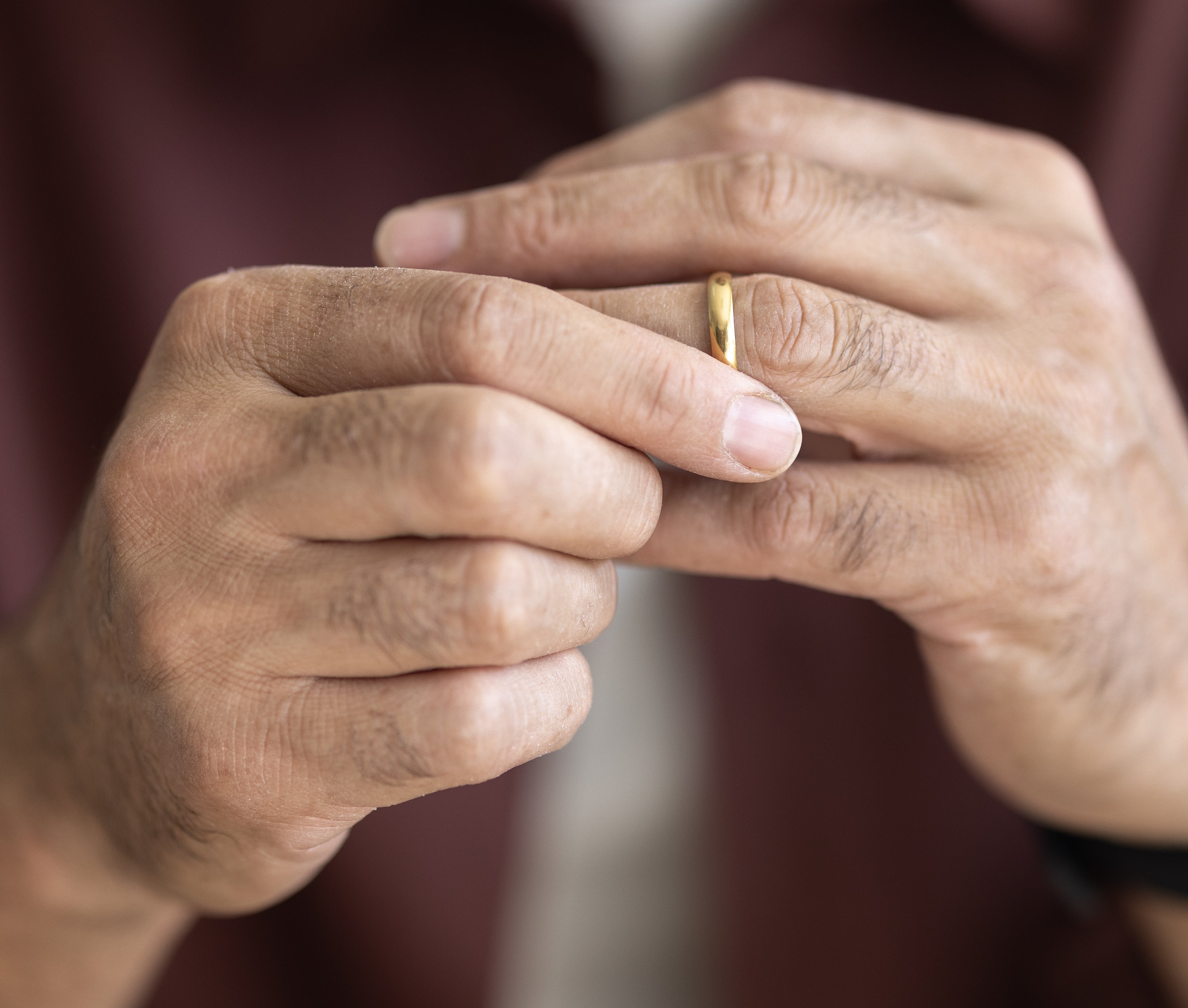 An older idiosyncratic with a beard is mildly holding a ring, wearing a watch, and a casual button-up shirt
