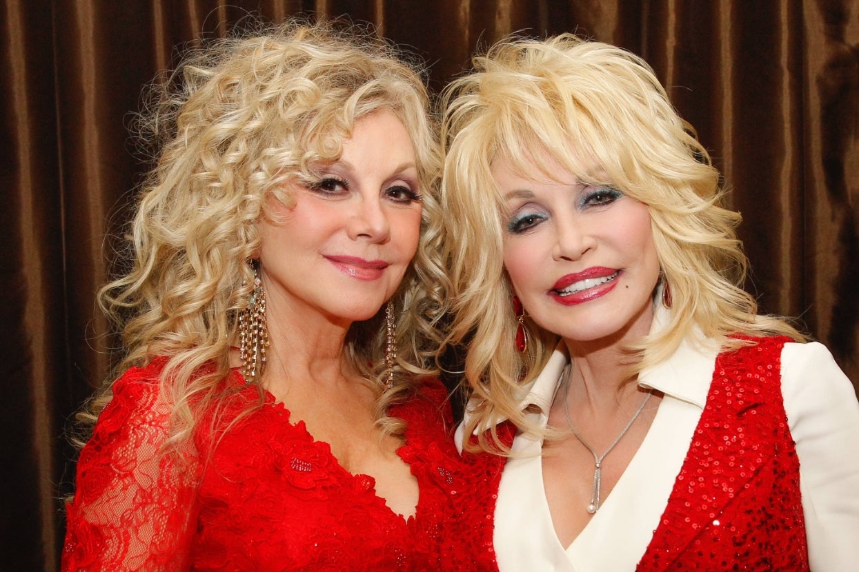 Two women with curly blonde hair smiling, wearing sequined red outfits