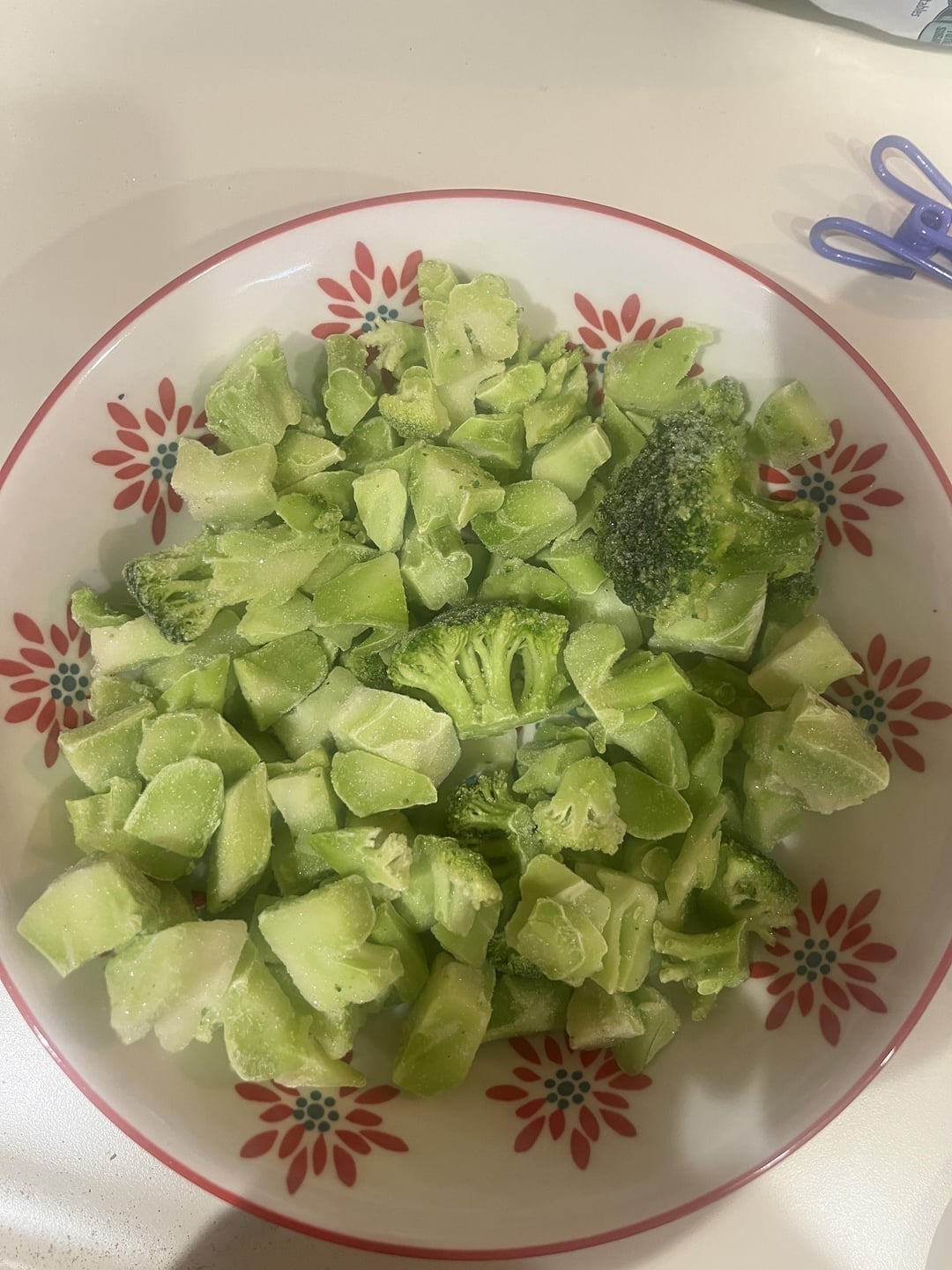 Bowl of frozen broccoli pieces connected  a flower-patterned plate