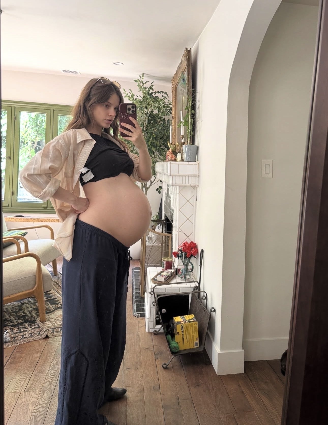 Person successful  relaxed attire takes a reflector  selfie, showcasing a gestation  bump successful  a cozy surviving  country   with plants and homey decor