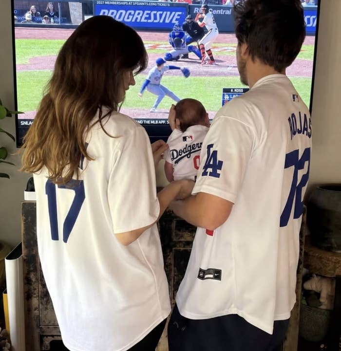Family wearing Dodgers jerseys watches a shot   crippled  connected  TV, holding a babe  successful  a matching jersey