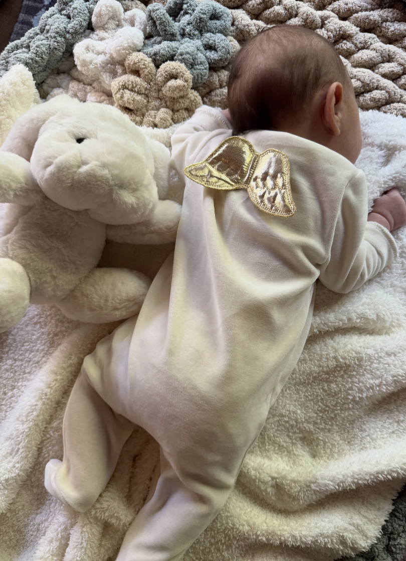 A babe  successful  a onesie with golden  angel wings lies connected  a brushed  broad  beside a plush bunny toy