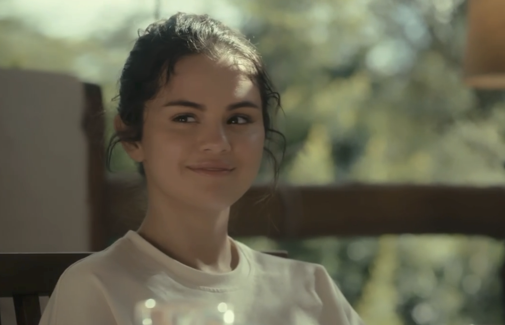 A woman with dark hair smiles gently while sitting outdoors in a relaxed setting