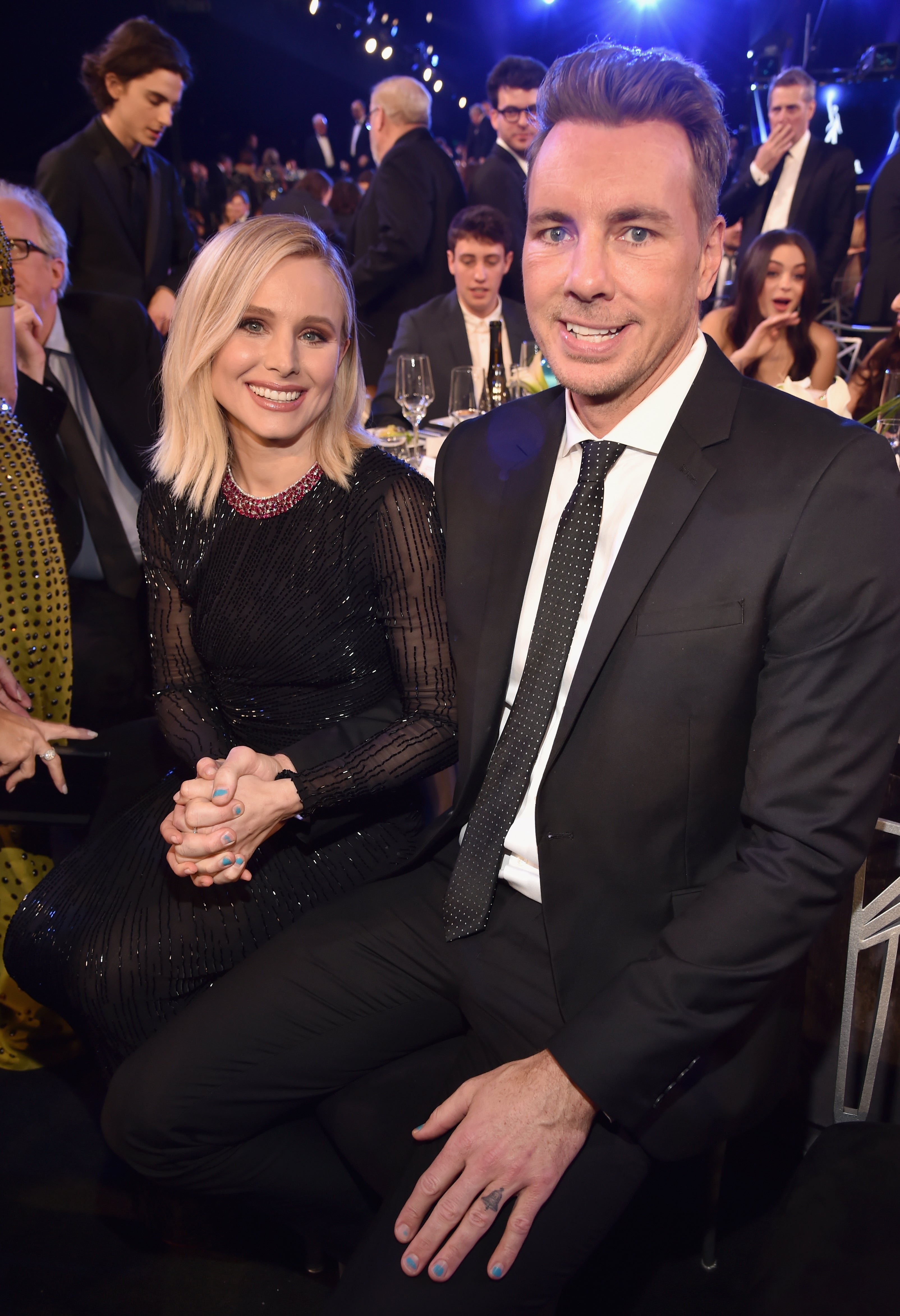 A smiling mates dressed successful elegant achromatic attire sits unneurotic astatine a ceremonial event, surrounded by different seated guests
