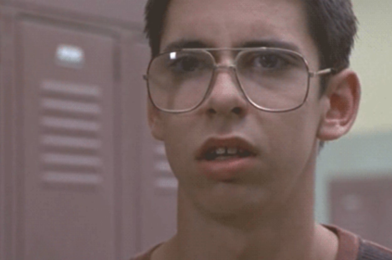 Person standing in front of lockers, wearing large glasses, with a surprised expression