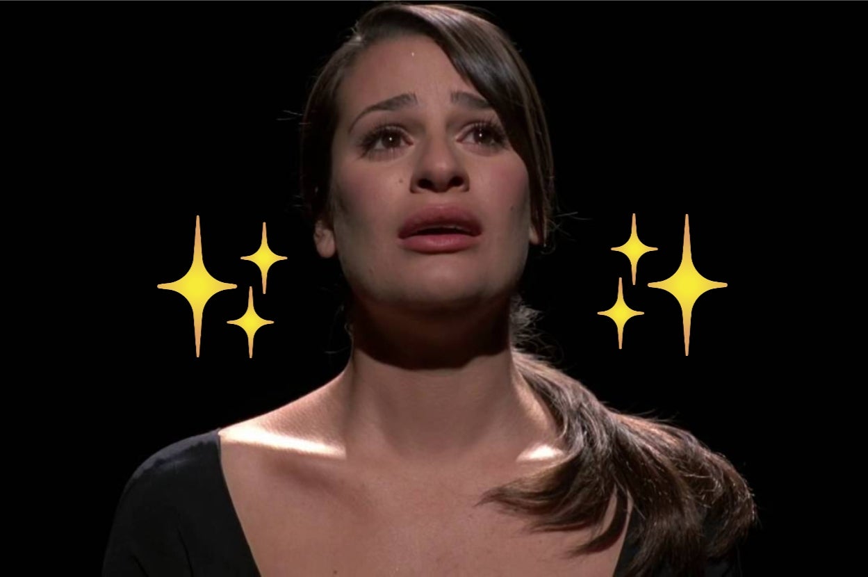 A person with long hair, wearing a scoop-neck top, looks emotional with sparkles around them against a black background