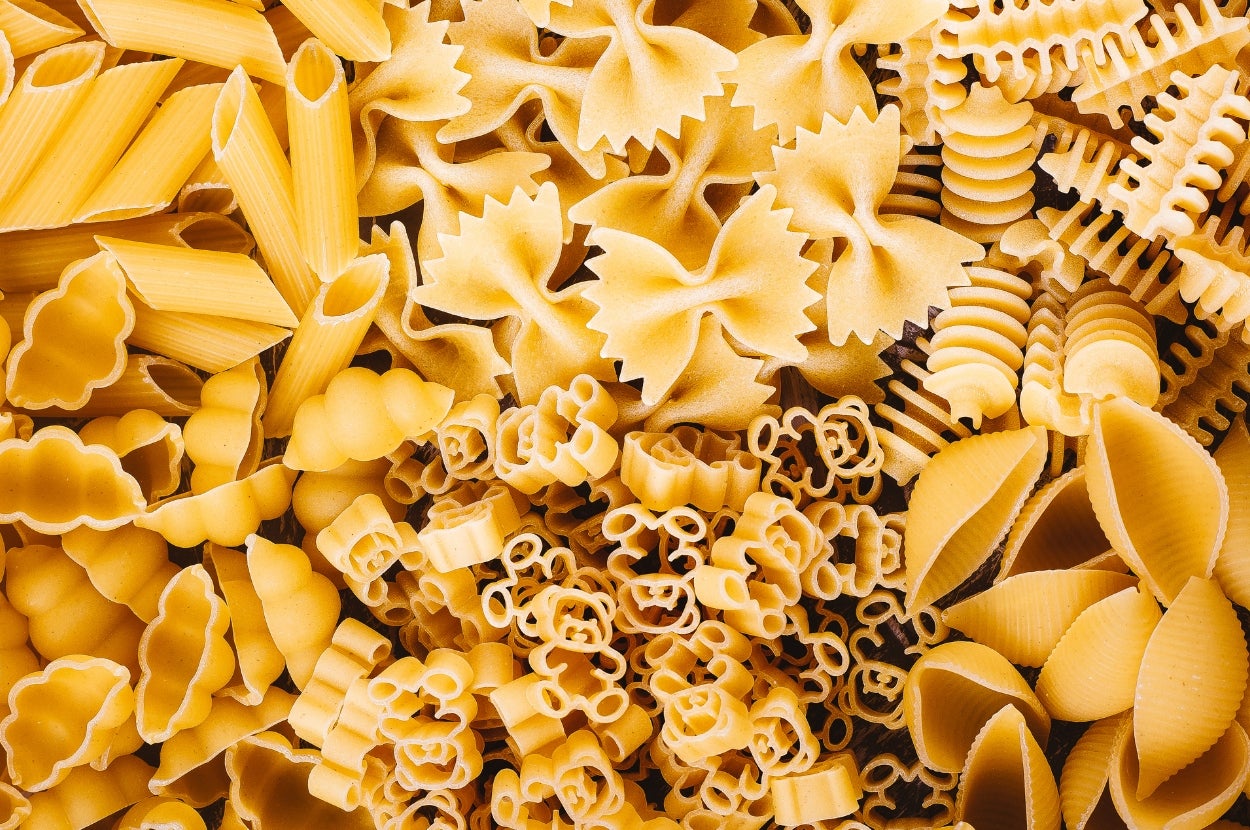 Various types of uncooked pasta, including penne, farfalle, rotini, and shells, arranged together