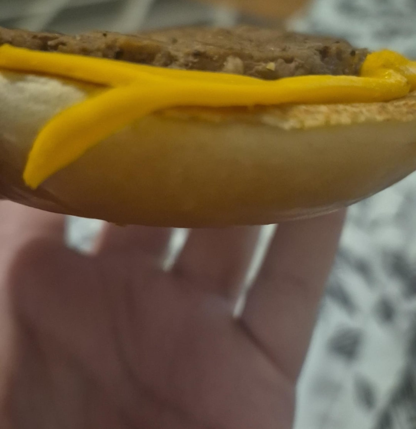 A manus  holding a hamburger with food  and a disposable   patty