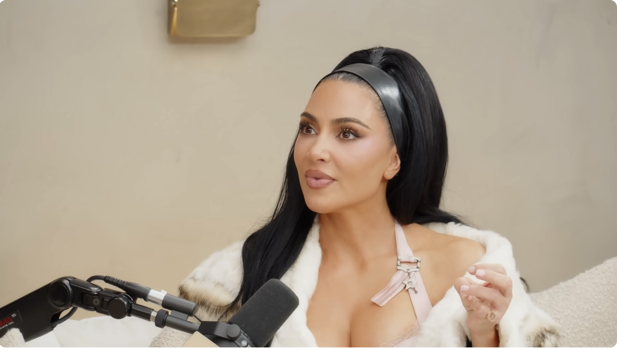 Person in a stylish fur-trimmed outfit and headband speaking into a podcast microphone