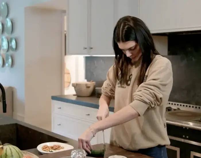 Person slicing a cucumber in a modern kitchen. Plates of food are on the counter