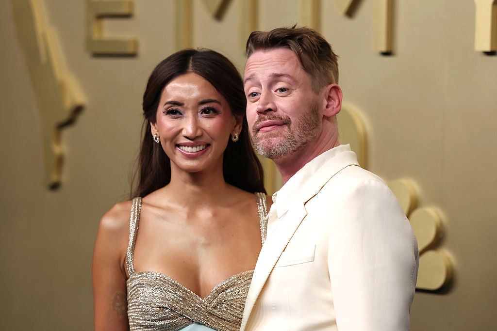 A woman in a shimmering gown and a man in a light suit pose on the red carpet at a celebrity event