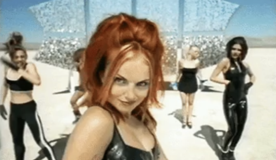 Group of women in sporty, futuristic outfits dance in a desert setting, with a sparkly backdrop