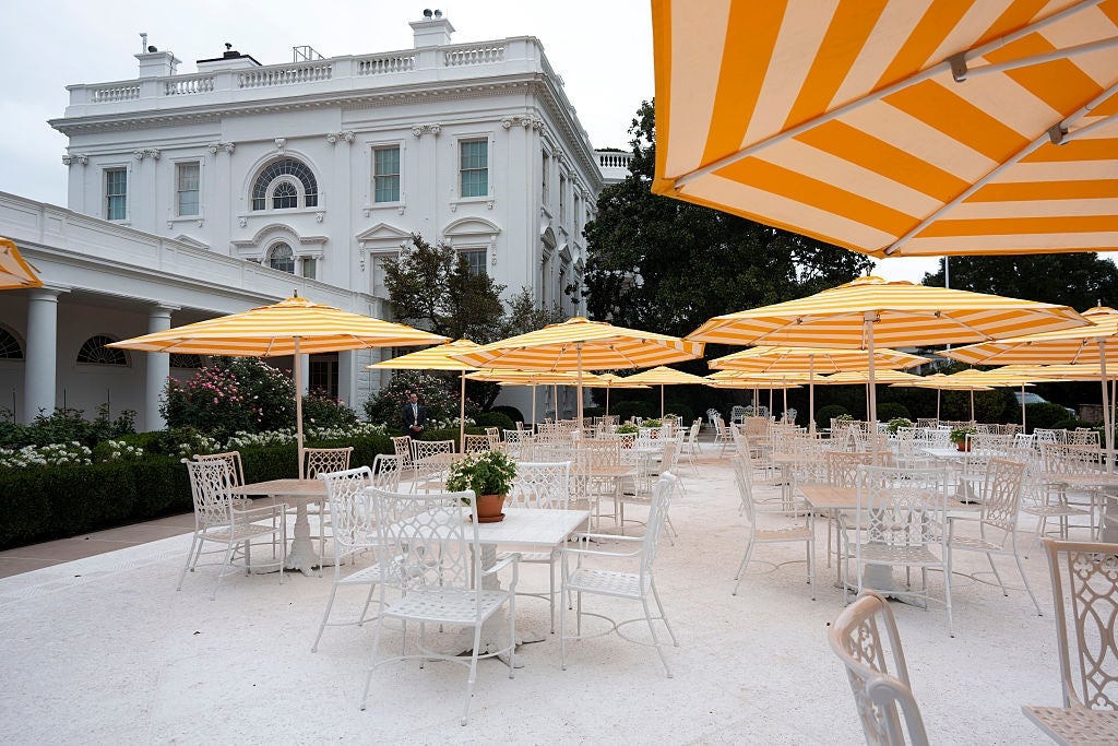 Outdoor patio with achromatic  tables and chairs, shaded by yellow-striped umbrellas, successful  beforehand   of a large, elegant achromatic  building