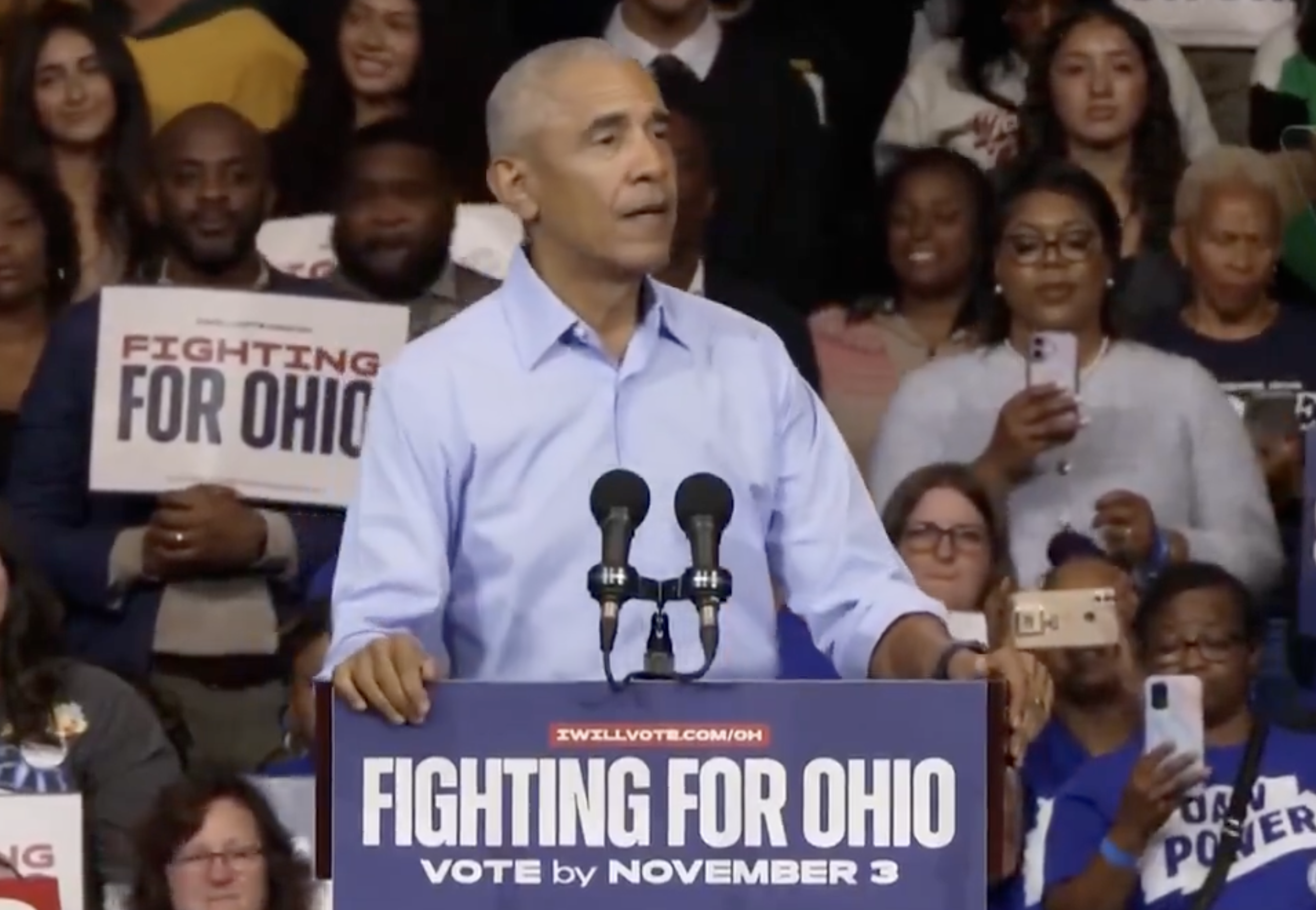 Person speaking astatine  a rally with "Fighting for Ohio" signage visible, surrounded by supporters holding signs and taking photos