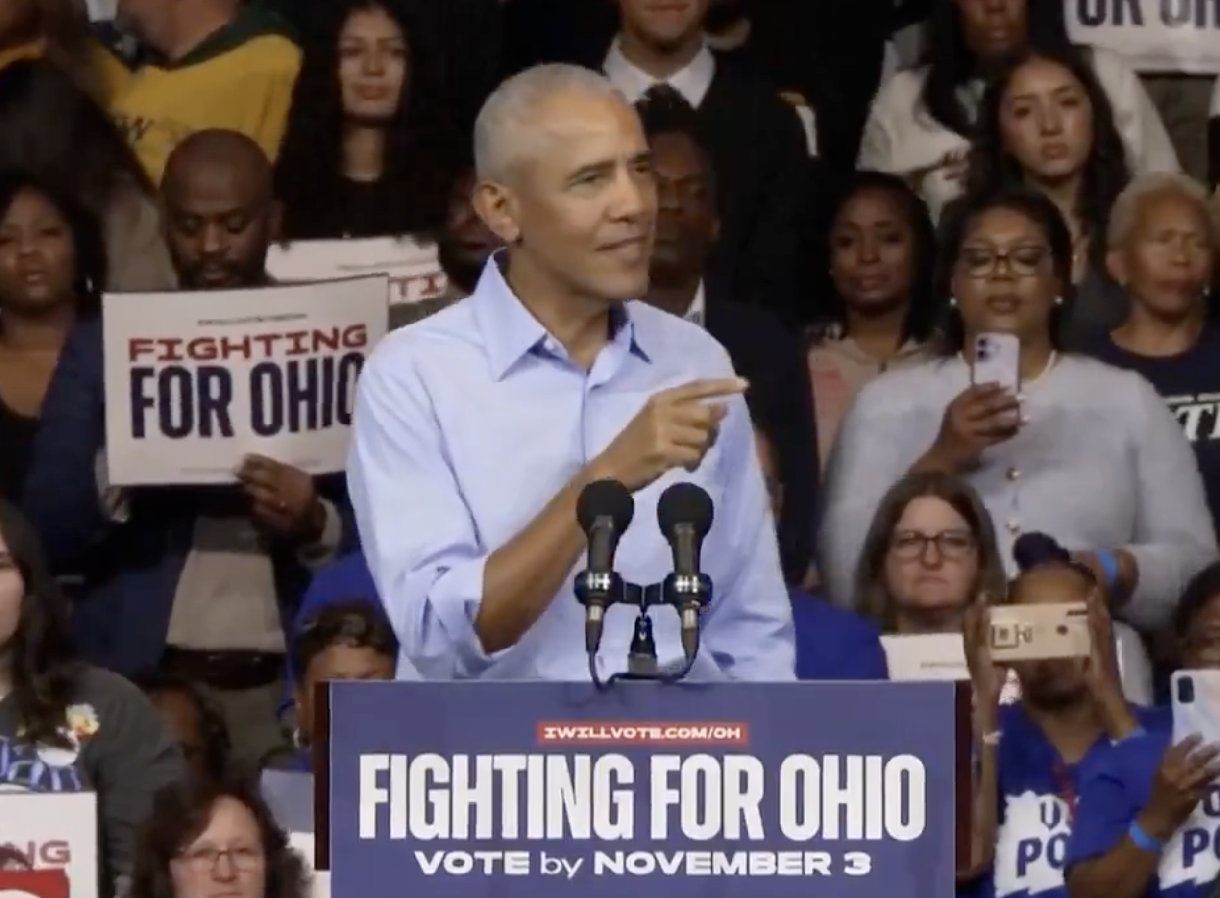 Person speaking astatine  an event, wearing a collared shirt, surrounded by radical   holding "Fighting for Ohio" signs