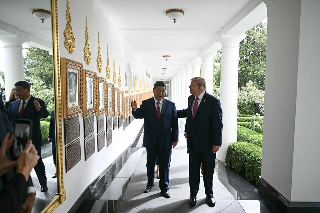 Two men successful  ceremonial  suits locomotion  down   a corridor lined with framed pictures, engaged successful  conversation, gesturing towards the images connected  the wall
