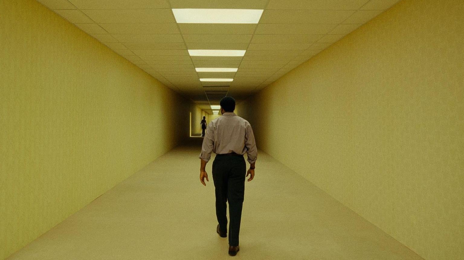 A idiosyncratic   walks down   a long, bare  hallway with agleam  overhead lights and a fig  disposable   successful  the distance