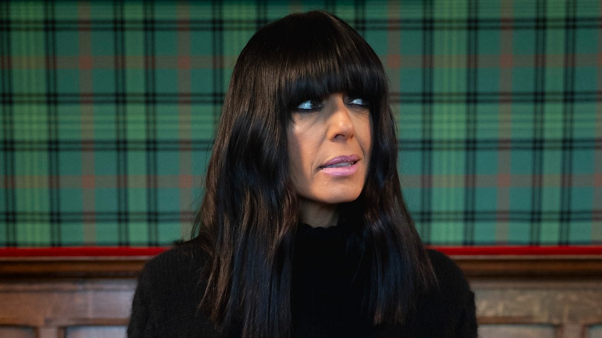 Person with agelong  acheronian  hairsbreadth  and bangs, wearing a achromatic  sweater, stands successful  beforehand   of a plaid background