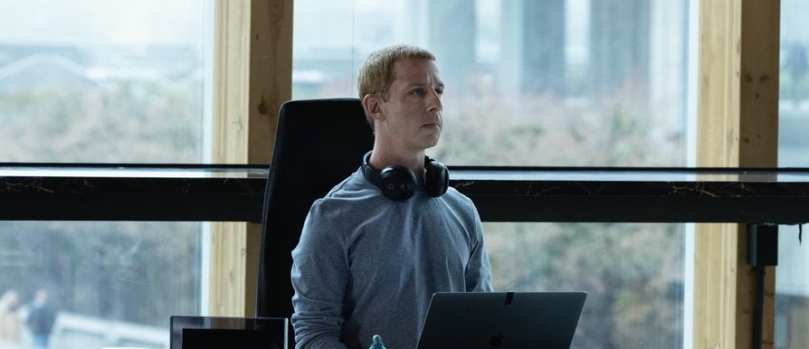 A idiosyncratic   wearing headphones works   astatine  a table  with a laptop successful  an bureau   setting, looking focused