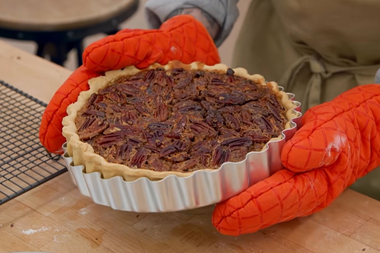 Person holding a pecan pie in an oven dish with quilted oven mitts