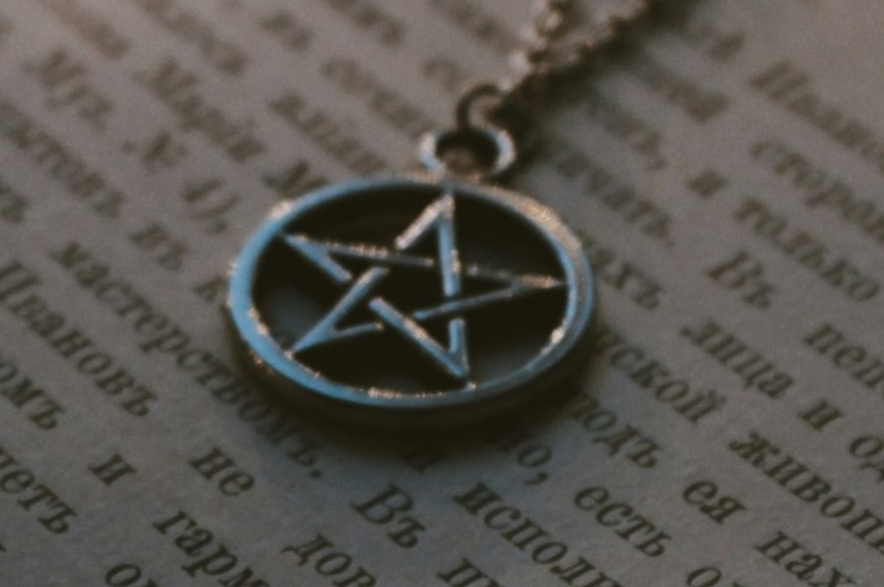 A metallic pentagram pendant lies on a page filled with text