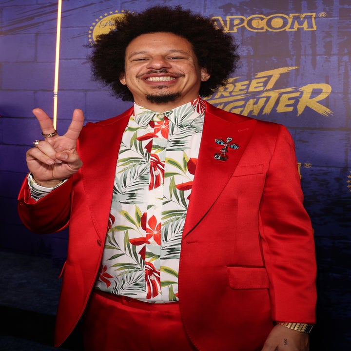Person in a stylish red suit with a tropical shirt poses, smiling, giving a peace sign at a "Street Fighter" event background
