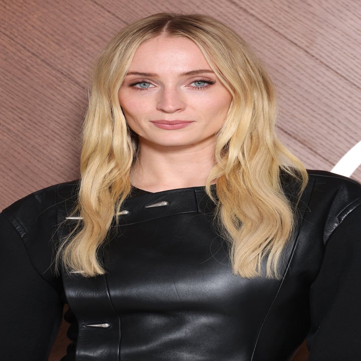 Person wearing a stylish black leather dress with long sleeves, posing in front of a textured backdrop