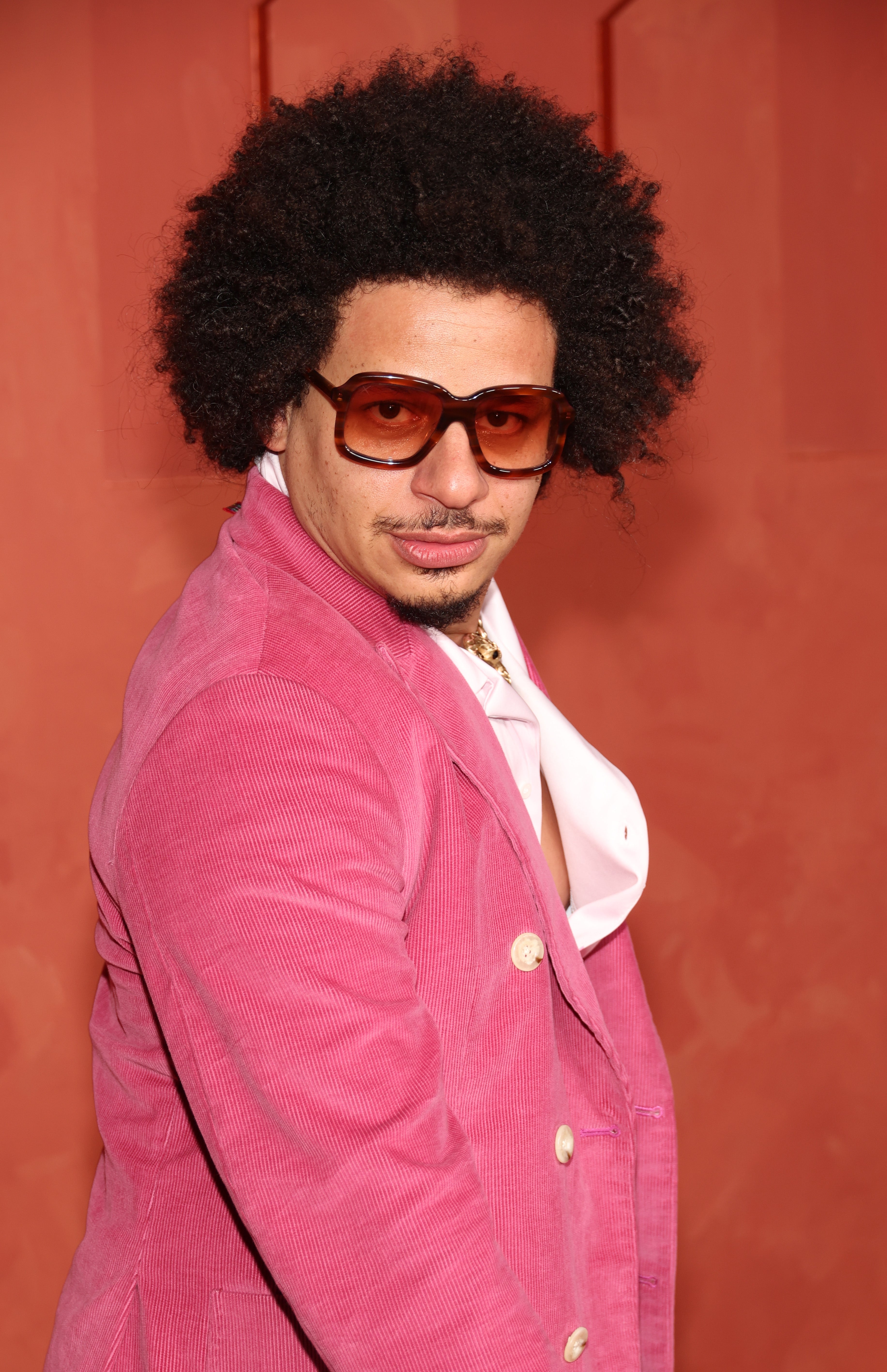 Eric Andre wears a pink double-breasted jacket and sunglasses, posing confidently