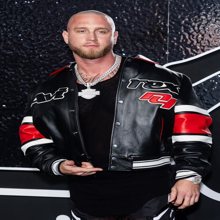 Person on red carpet wearing a black and red leather jacket, matching pants, and high-top sneakers