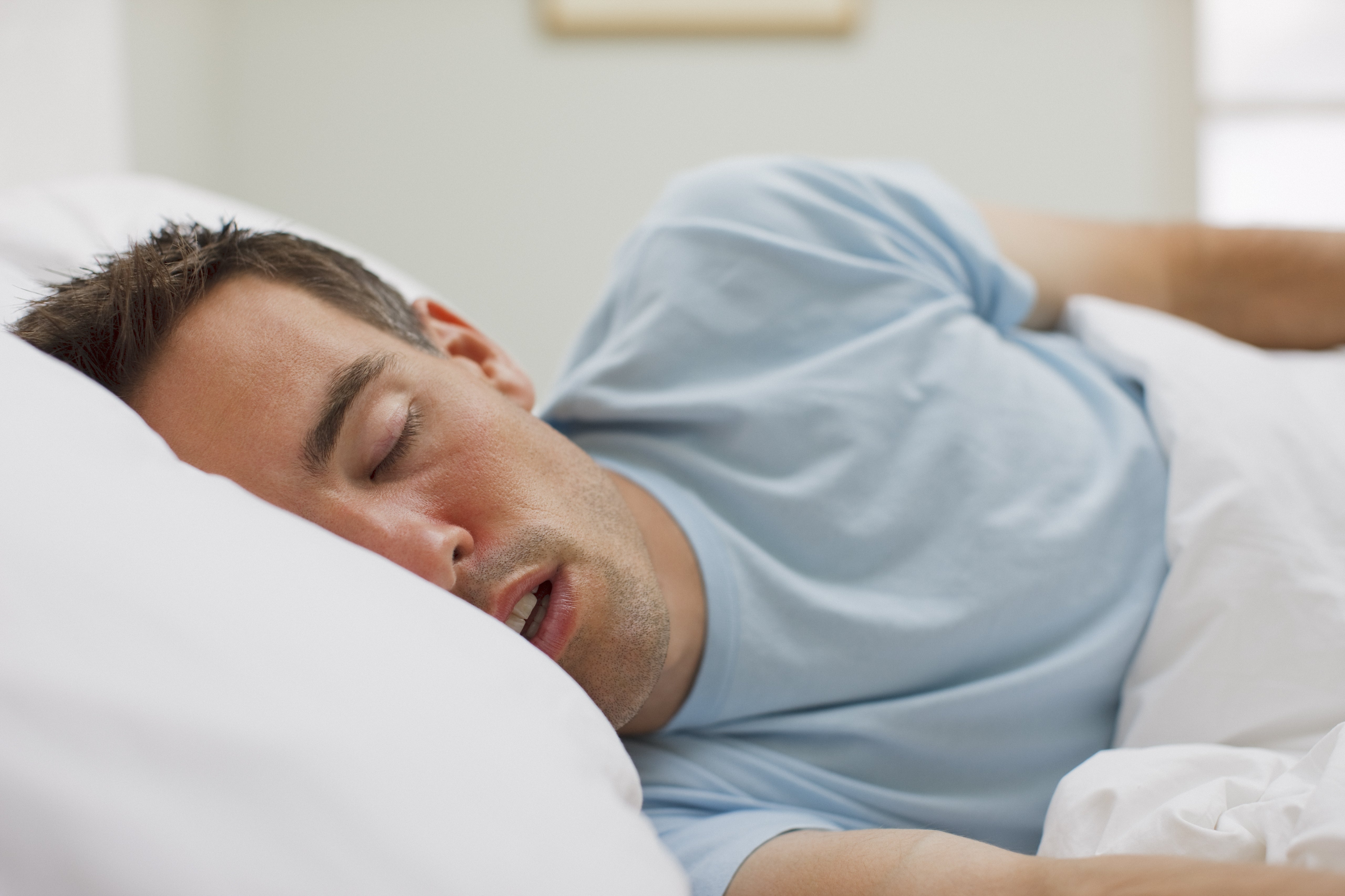 Person sleeping peacefully in bed, partially covered by a white blanket, wearing a light shirt