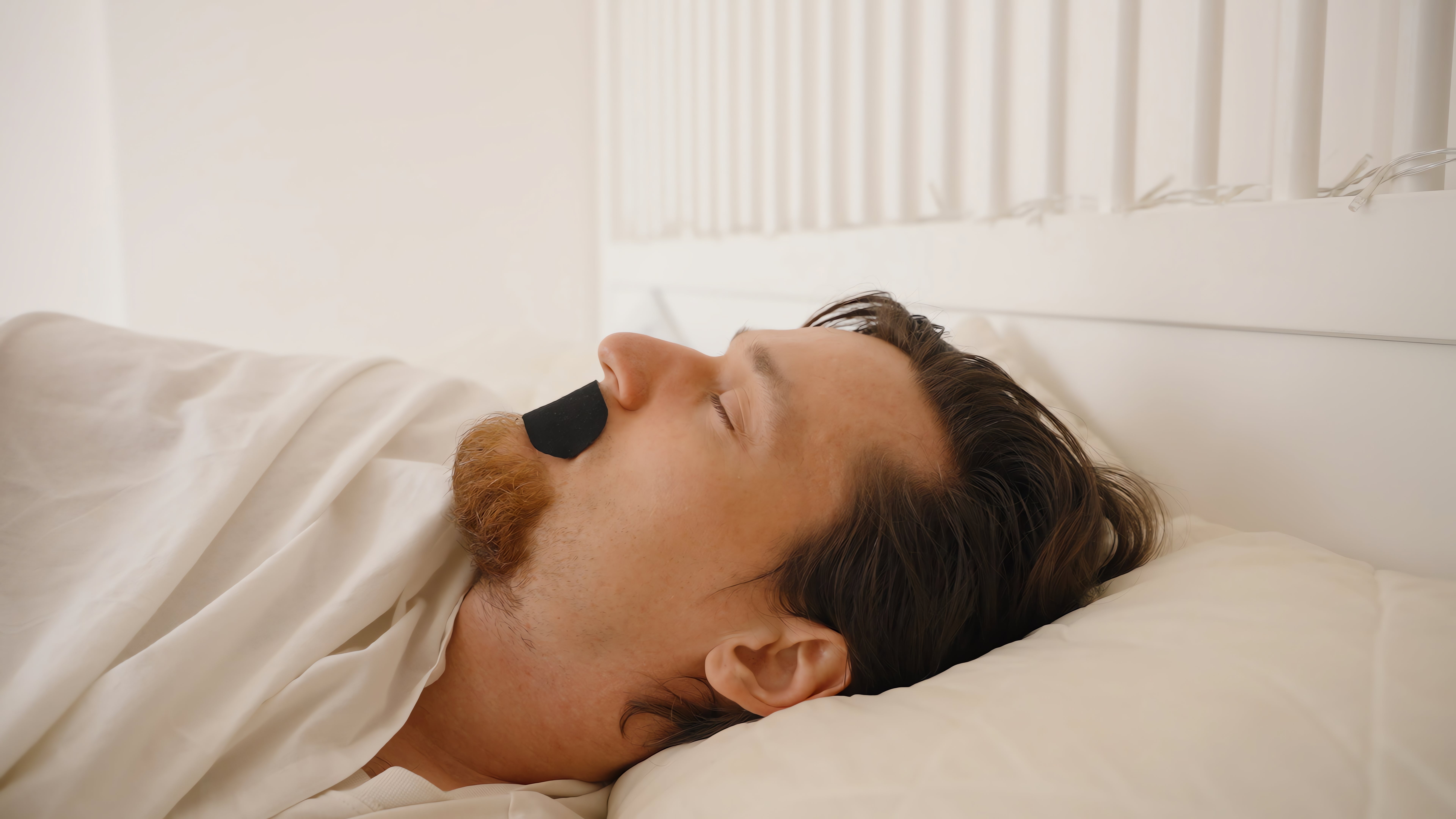 Person sleeping in bed with a strip over their mouth, likely promoting nasal breathing or as a sleep aid