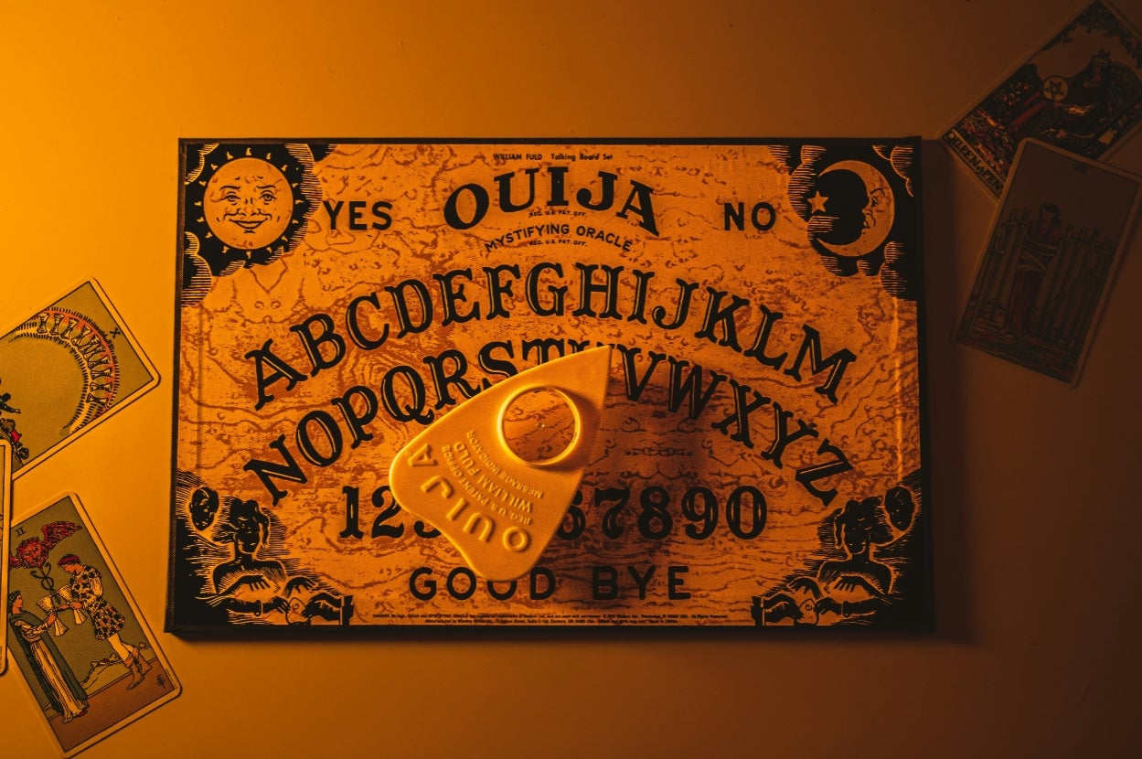 Ouija board with planchette on top, surrounded by tarot cards, set against a warm, dimly lit background