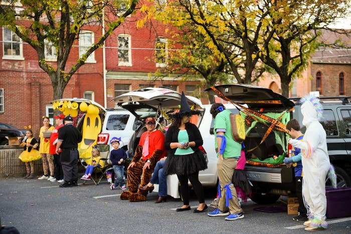 People in costumes participate in a trunk-or-treat event in a parking lot with decorated car trunks