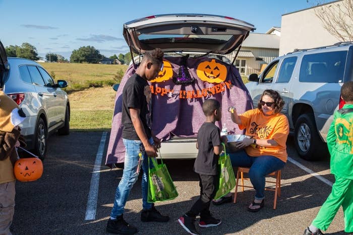 Kids receiving candy at a trunk-or-treat event from a decorated car with Halloween banners and pumpkins