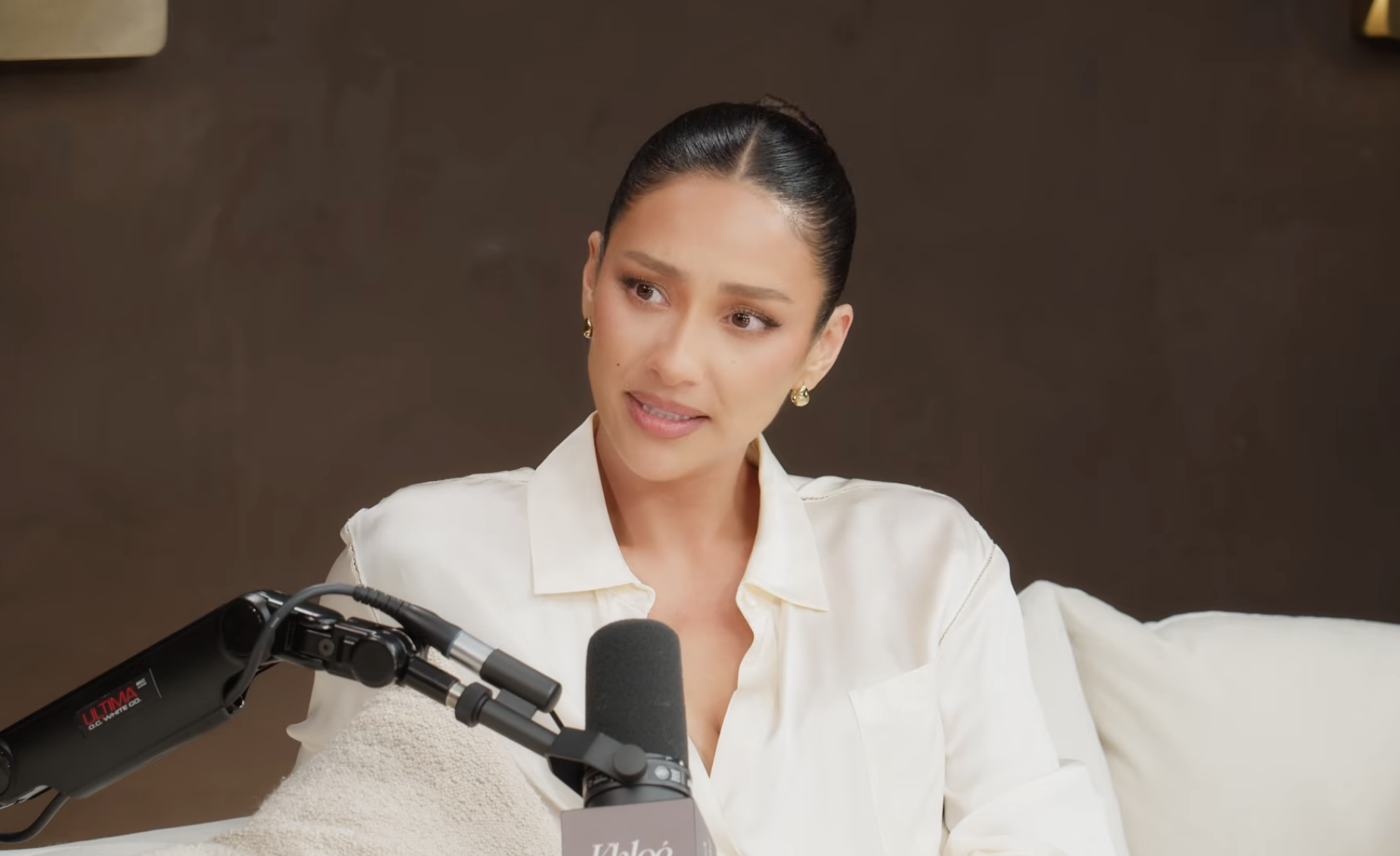 Person in a light blouse speaking into a microphone during a podcast or interview setting