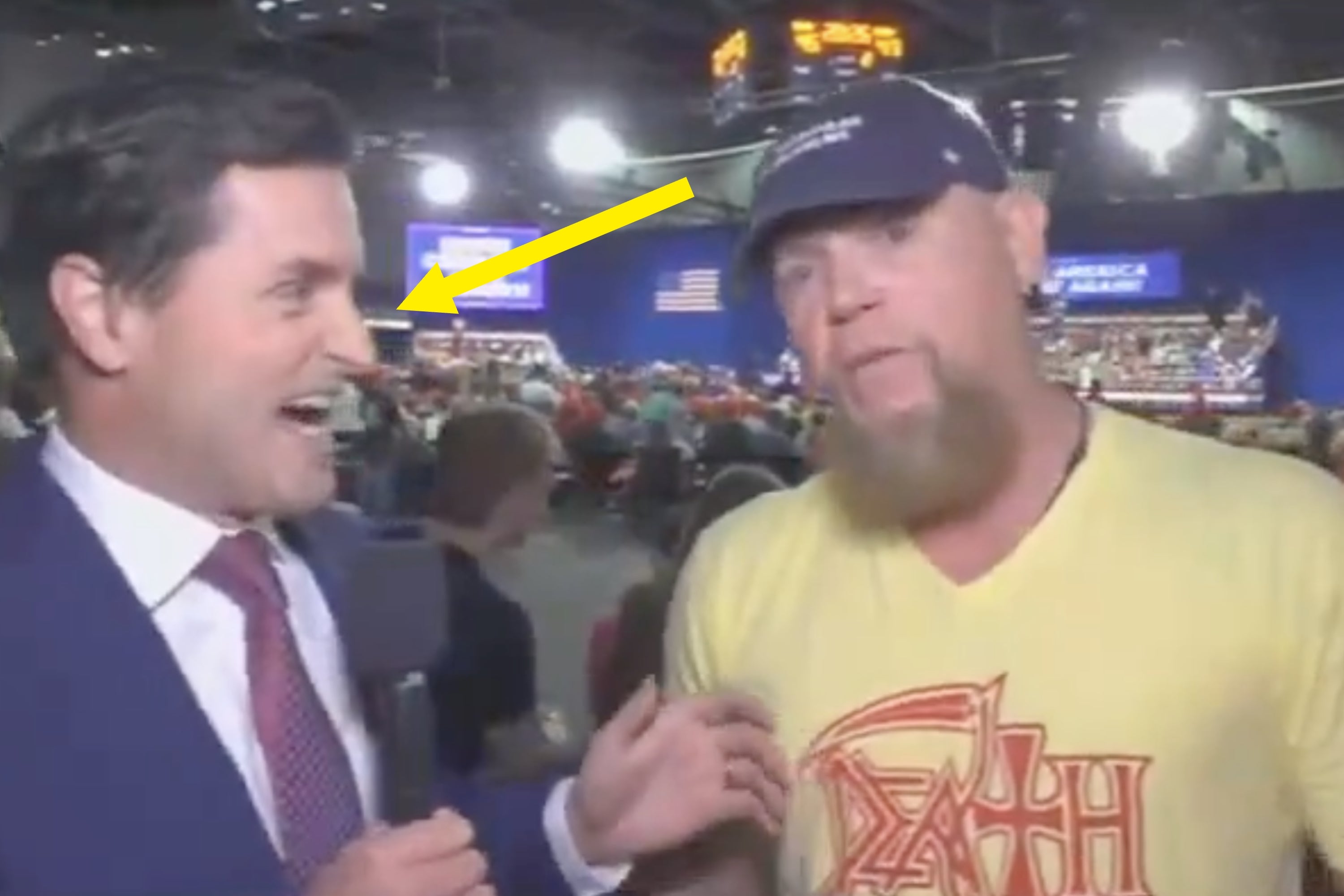 News reporter interviewing a man in a graphic T-shirt and cap at a large indoor event