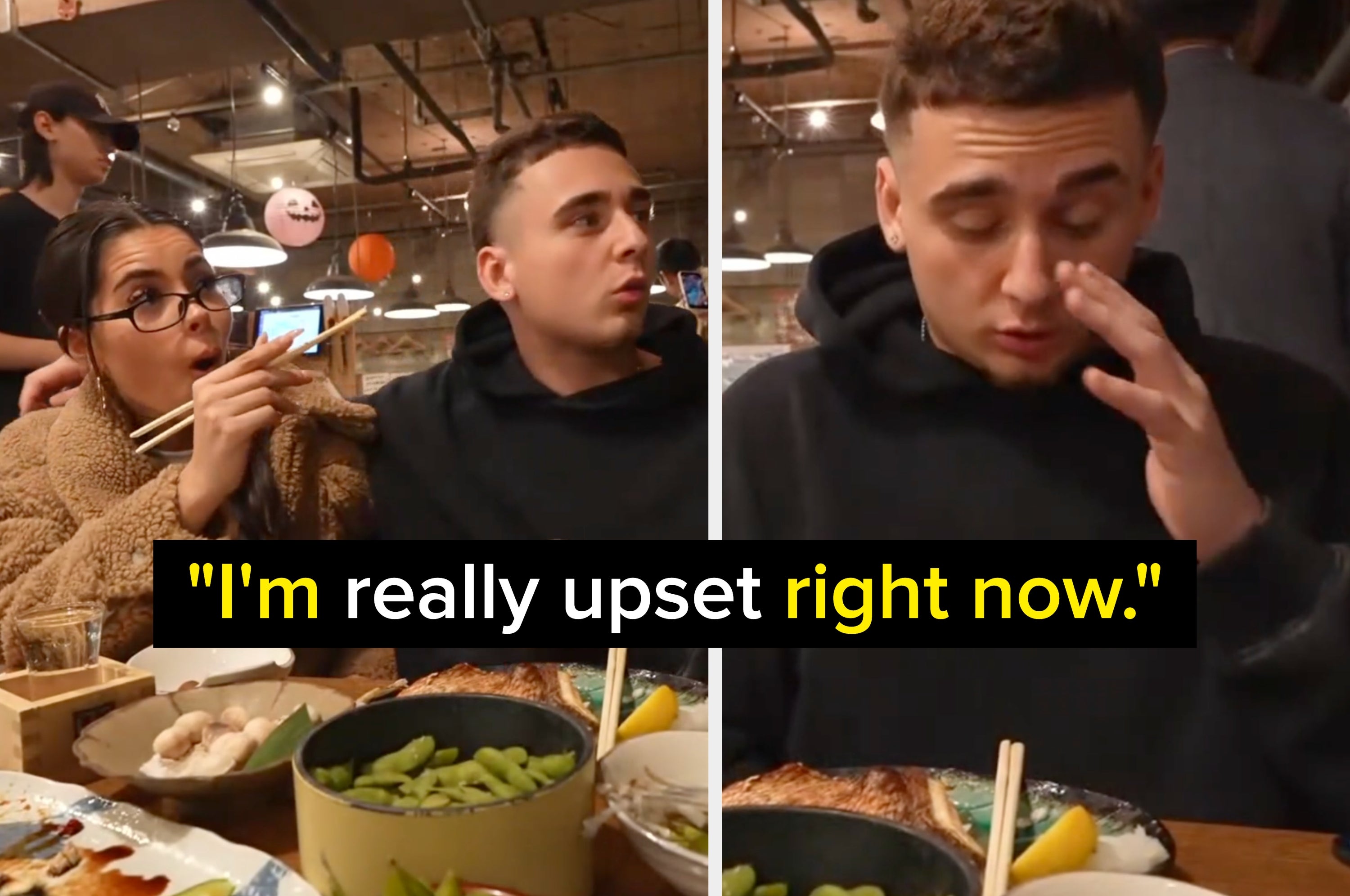 A person, surprised, holds chopsticks while another looks embarrassed, wiping their eyes at a restaurant table with various dishes