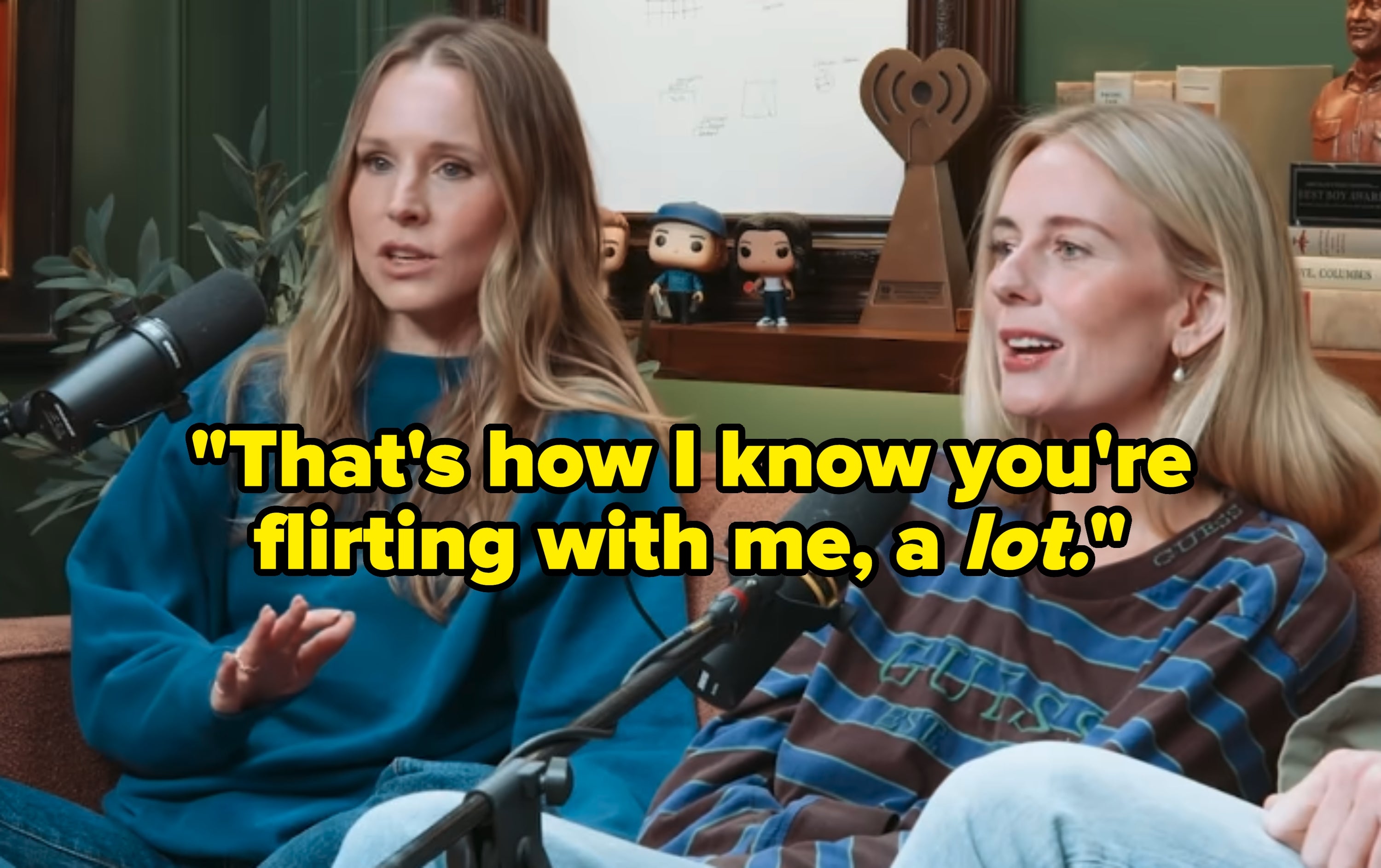 Kristen Bell and Justine Lupe sitting on a couch, speaking into microphones during a podcast recording. They appear engaged in conversation