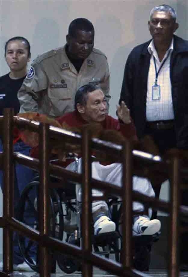 Panama's former strongman Manuel Noriega gesturing while being carried in a wheelchair by a police officer inside El Renacer prison, on the outskirts of Panama City -- December 11, 2011. (AP Photo/Esteban Felix)