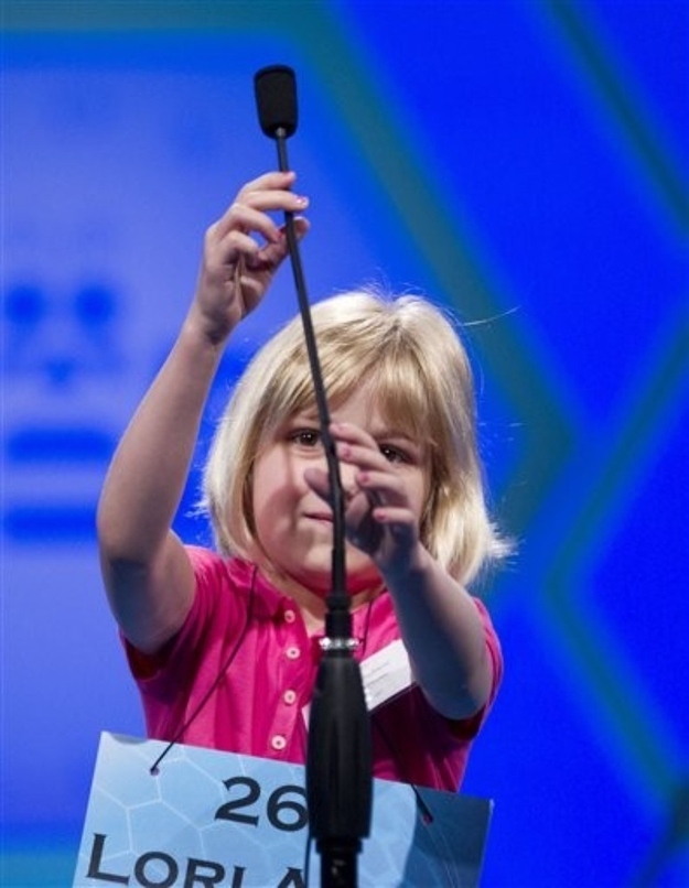 Six-year-old Lori Anne Madison, of Woodbridge, Va., the youngest contestant in the history of the National Spelling Bee, reaches for the microphone during the second round, Wednesday, May 30, 2012, in Oxon Hill, Md.