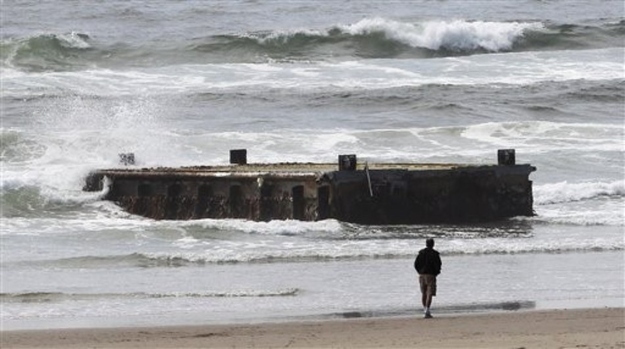 A man looks at the massive dock with Japanese lettering that washed ashore on Agate Beach Wednesday, June 6, 2012, in Newport, Ore. It floated ashore on the beach after being torn loose from a fishing port in northern Japan by last year's tsunami and drifted across thousands of miles of Pacific Ocean, a Japanese Consulate official said Wednesday.