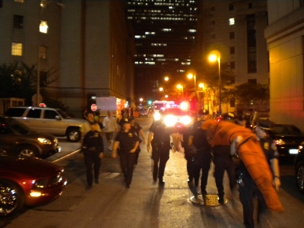 A group of police officers presses the march onward, carrying the rolled-up net.