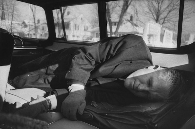 George Romney sleeps in a station wagon's built-in bed, March 1958.