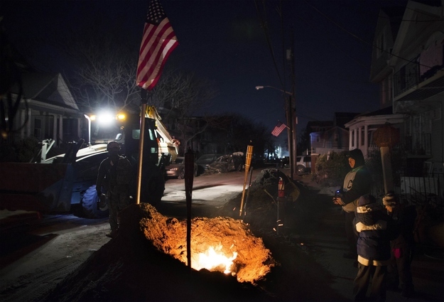 Residents look at the National Guard drive through the Rockaway Beach neighborhood as they stand near a fire listening to the radio for news of the U.S. presidential election, while still missing access to power in New York's Queens borough, November 6, 2012.